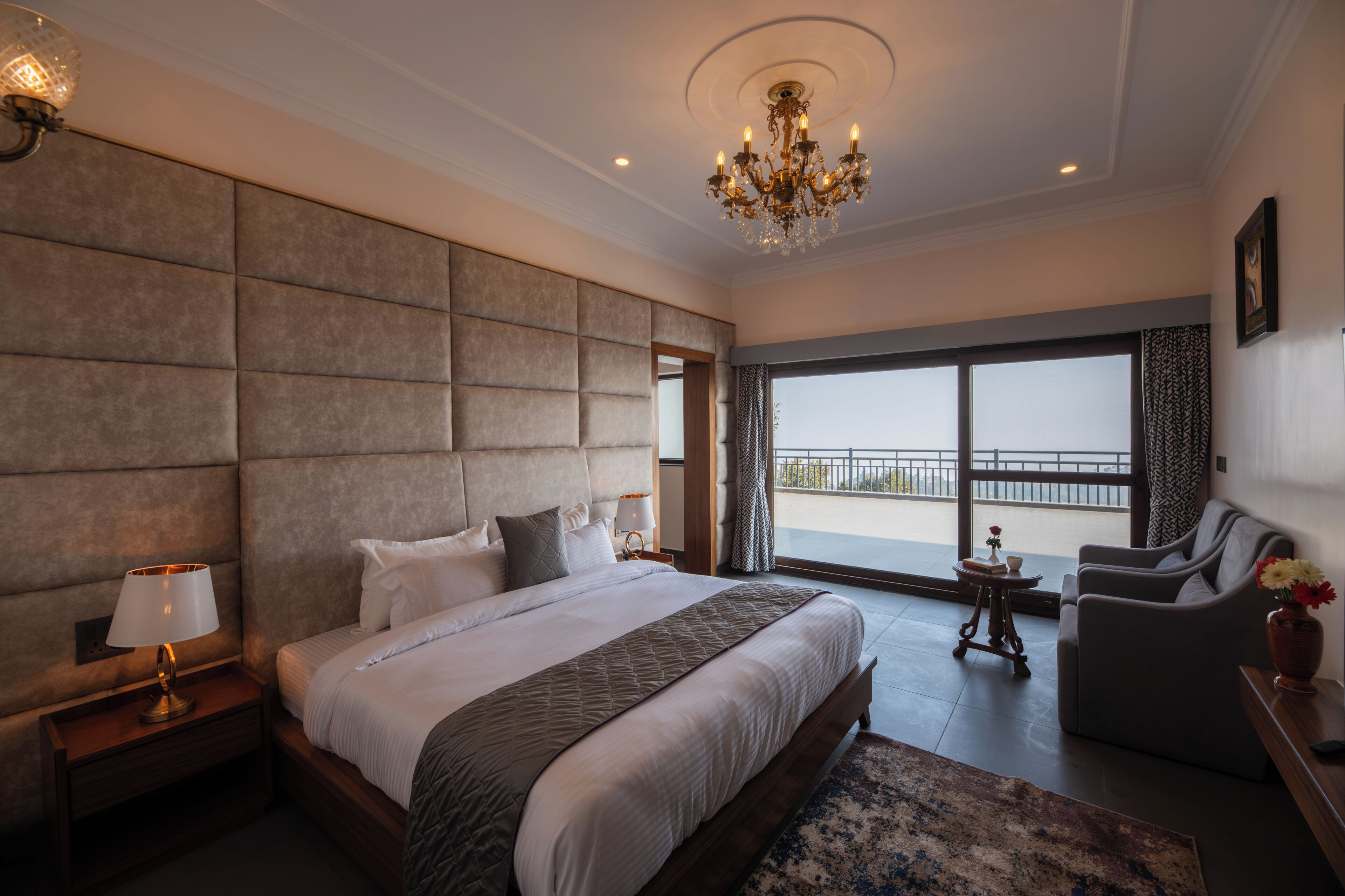 Un dormitorio amplio con una cama grande, un candelabro, un balcón con vistas y una zona de estar.