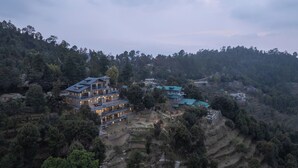 A multi-story building with a modern design, surrounded by dense forest and terraced fields.