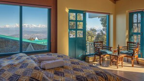 A room with a bed, two chairs, a table, and a view of mountains.