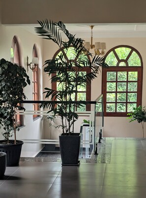 A spacious indoor area with large windows, potted plants, and a modern staircase. - Dharohar Retreat Mukteshwar (Kosiyakutoli)