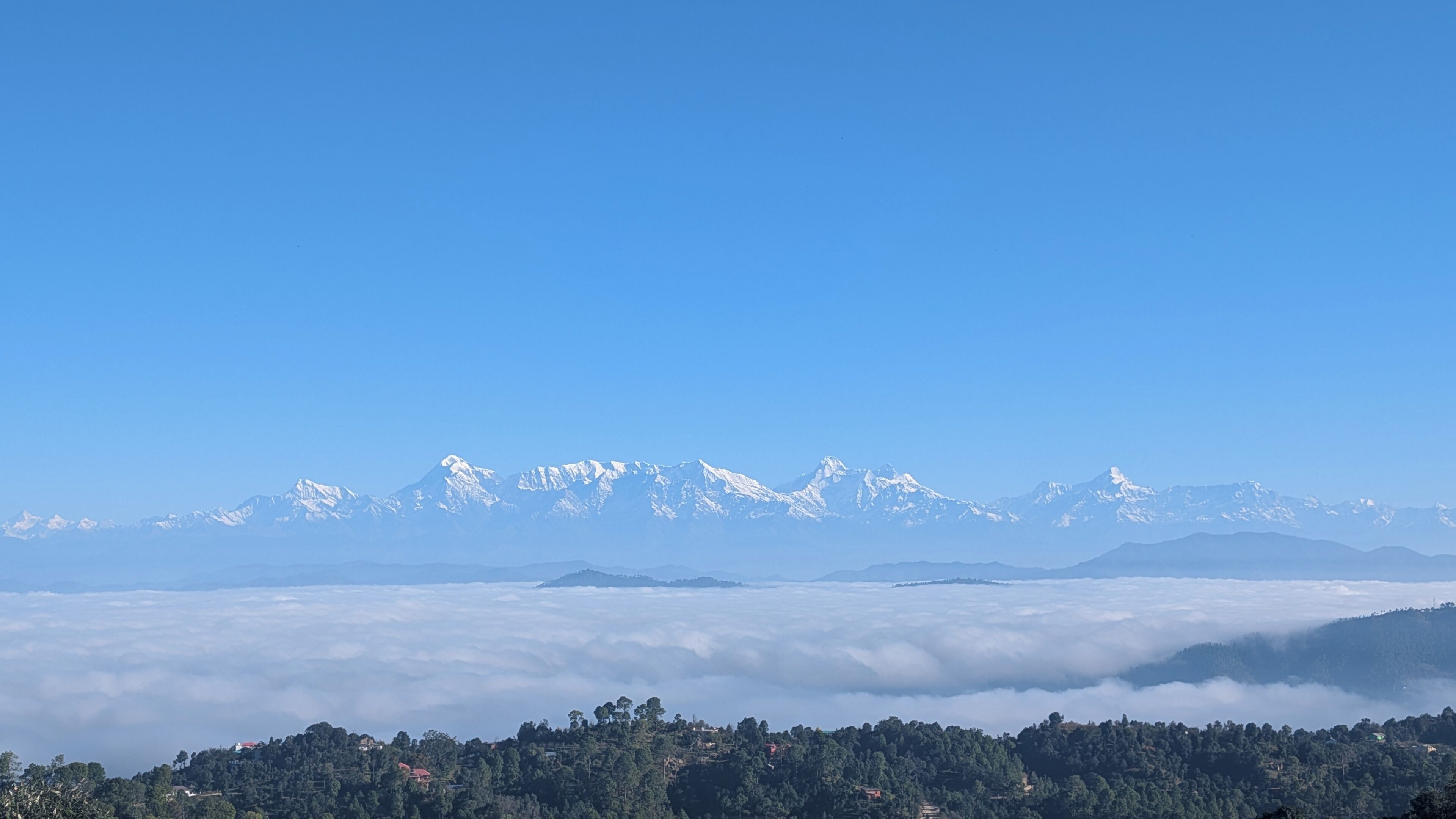 A mountain range with snow-capped peaks and a forested valley below.
