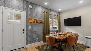 Uma área de jantar com uma mesa posta para quatro pessoas, uma televisão na parede e um papel de parede estampado.