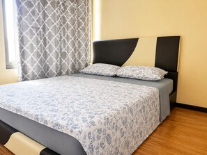 A neatly made bed with a floral bedspread, a headboard with a geometric pattern, and a window with patterned curtains. - Radiance Manila Bay · Pet-Friendly 100sqm 2BR (Pasay City)