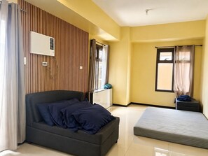 Una habitación con cama, mesita de noche, ventana con cortinas y aire acondicionado de pared.
