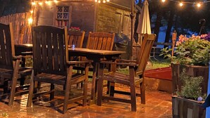 Ein hölzerner Essbereich im Freien mit Tisch, Stühlen, einem roten Sonnenschirm und Lichterketten.