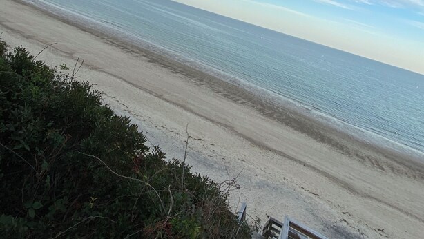Ein Strand mit einer Holzkonstruktion, möglicherweise ein Deck oder Steg, und freiem Blick auf das Meer.