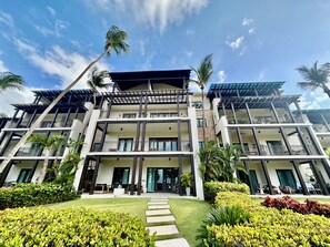 Ein mehrstöckiges Hotel mit Balkonen, einem zentralen Eingang und umgebender Bepflanzung.