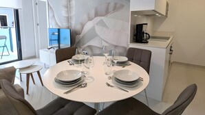 Een moderne eetruimte met een ronde tafel voor vier personen, omringd door donkere stoelen. Boven hangt een grote hanglamp, en in de achtergrond is een keuken zichtbaar.