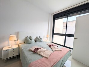 Ein Schlafzimmer mit einem Bett, zwei Nachttischen, einem Fenster und einer Tür.