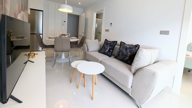 Een moderne woonkamer met een bank, twee witte ronde tafels en een eethoek met stoelen.