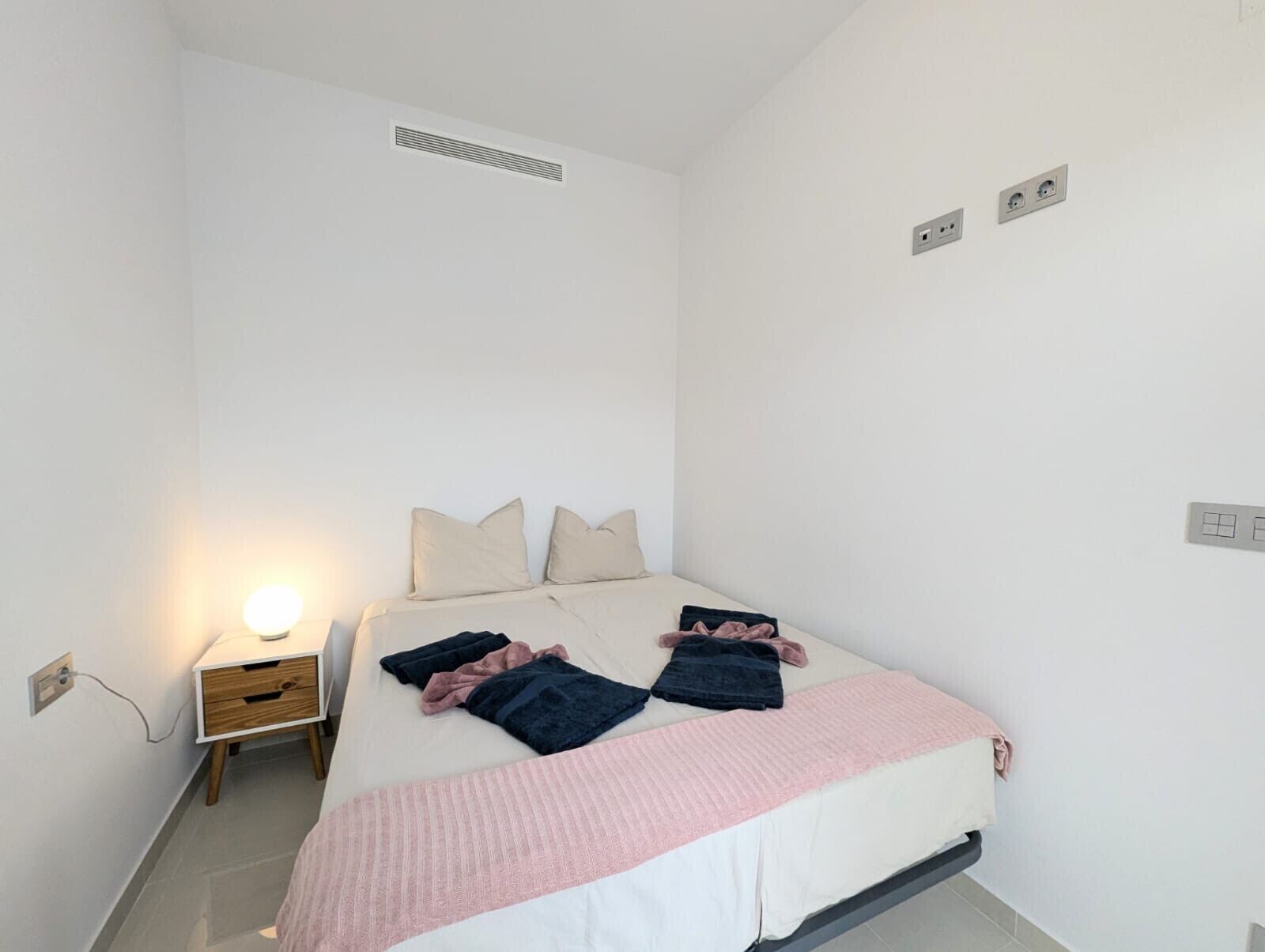 Un dormitorio con cama, mesita de noche, lámpara y enchufes.