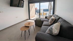 A modern living room with a sofa, two small tables, a flat-screen TV, and a large sliding glass door leading to an outdoor area.