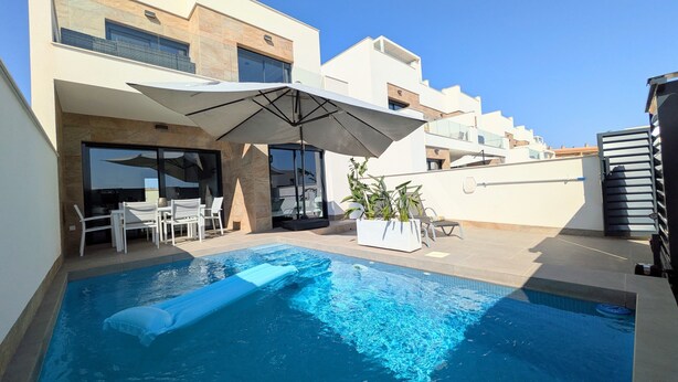 A modern outdoor pool area with a clear blue pool, white lounge chairs, and a large umbrella.