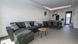 A modern living area with a sofa, a small coffee table, and a dining area with chairs and a kitchen in the background.