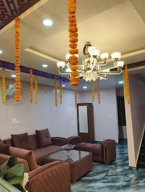 A modern living room with a sectional sofa, a glass coffee table, and a chandelier. - Hotel Surbhi International Dhanbad (Gobindpur)