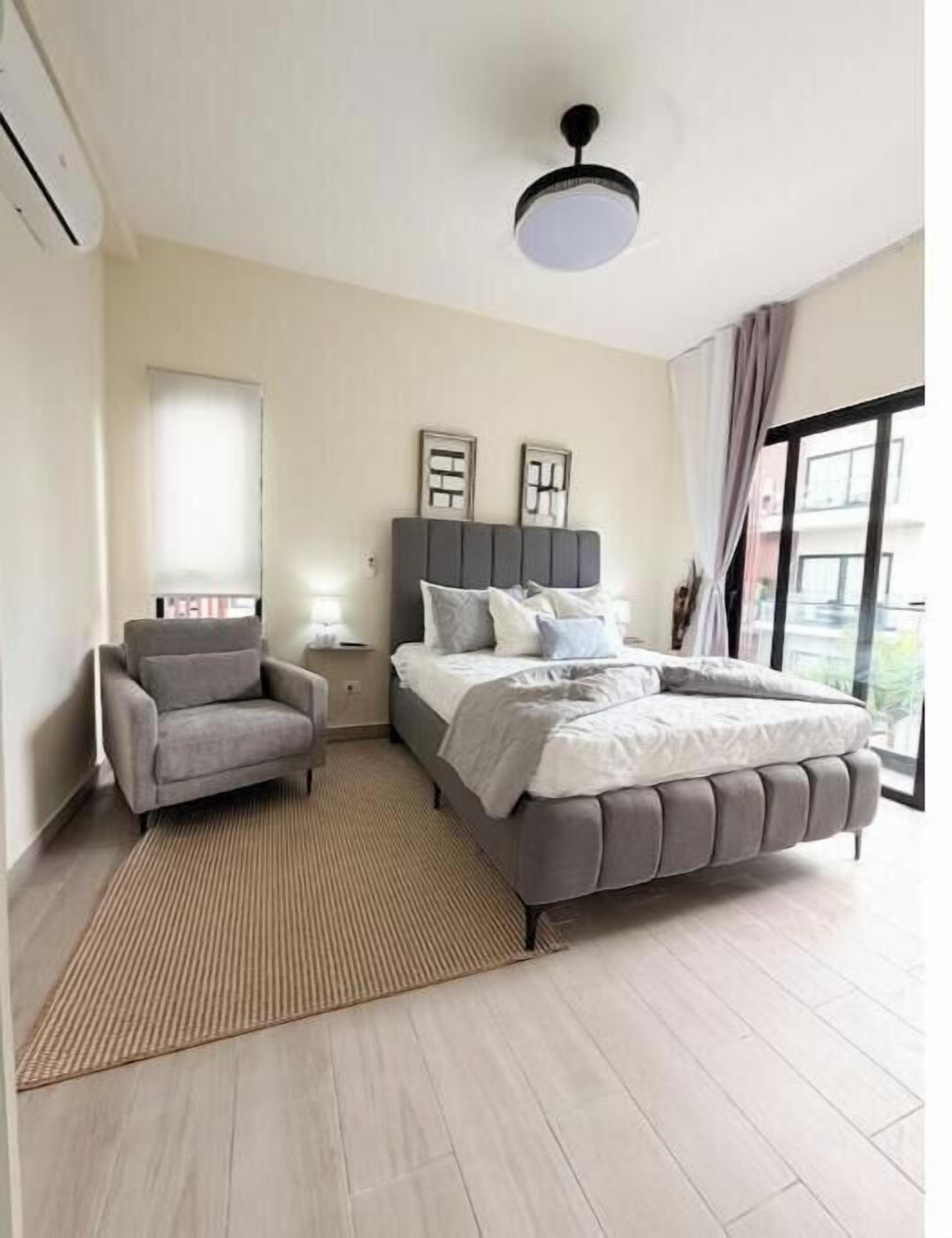 A modern bedroom with a bed, a chair, a bedside table, and a large window.