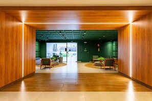 En modern entréhall med träväggar, en central sittgrupp med stolar och ett bord, och utsikt genom en glasdörr till ett utomhusområde.