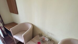 A room with two beige chairs, a small wooden table with a red object, and a wall-mounted light fixture.