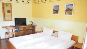 A hotel room with a large bed, a desk with a television, and two framed pictures on the wall.