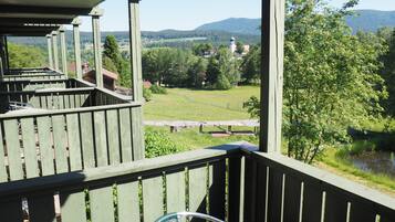 A wooden balcony with a view of a green landscape, a bench, and a chair.