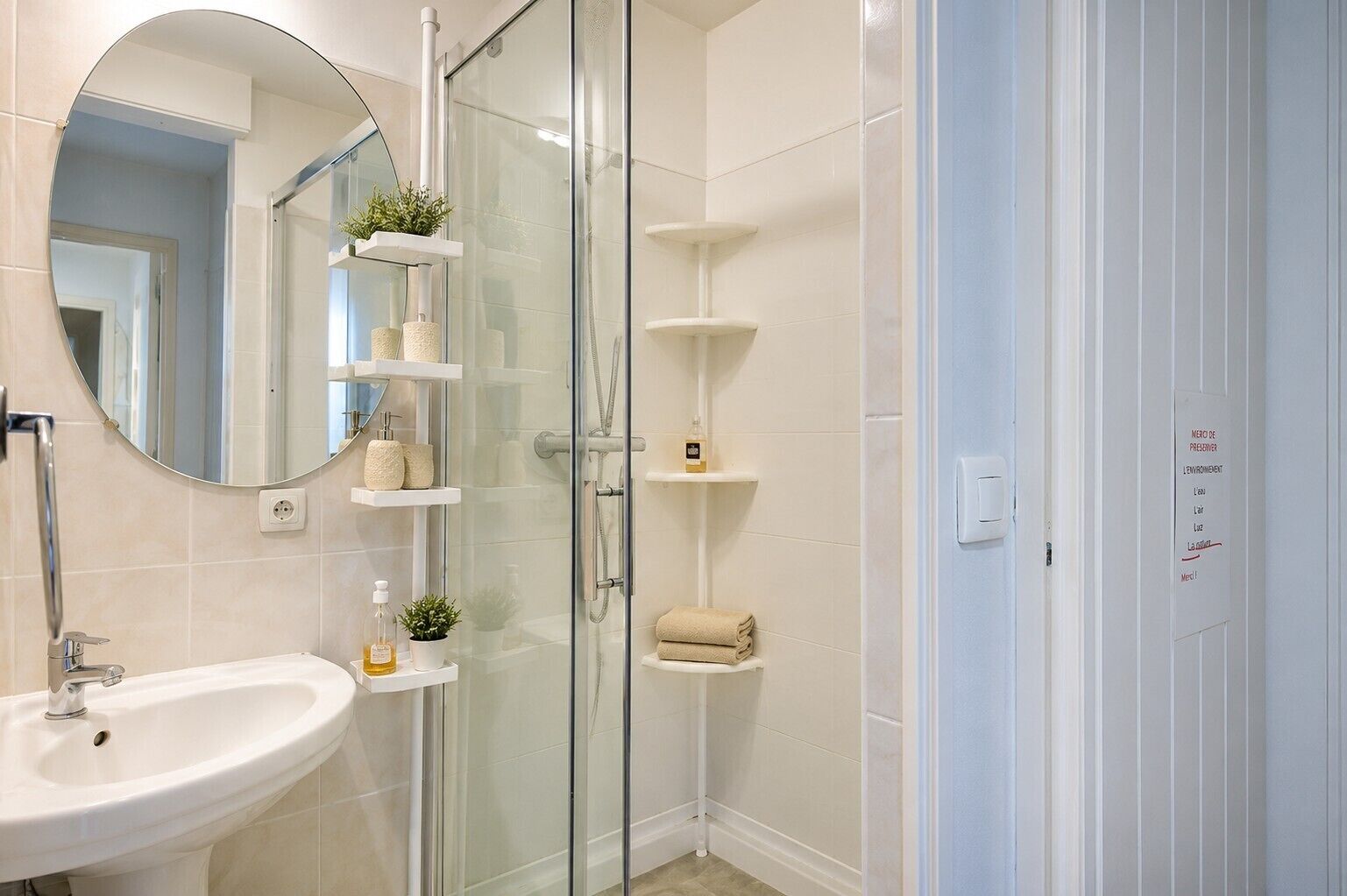 A bathroom with a glass-enclosed shower, a sink, and shelves with toiletries.