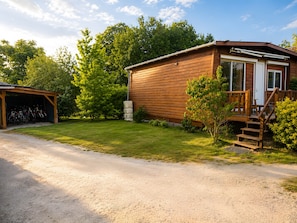 Une cabane en bois avec un garage fermĂ©, un porche Ă lâavant et une allĂ©e gravillonnĂ©e.