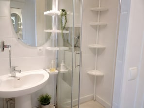 Une salle de bain moderne avec un lavabo blanc, une douche en verre et plusieurs étagÚres.