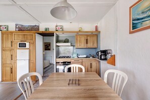 Cocina compacta con armarios de madera, microondas, estufa y comedor con mesa y sillas.
