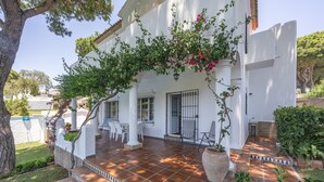 A white building with a tiled patio, steps leading to the entrance, and a covered seating area. - Villa Jacaranda Chiclana, Private Pool and Barbecue (Chiclana de la Frontera)