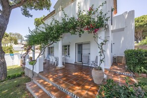 Un bâtiment blanc doté d’un patio carrelé, d’un escalier menant à l’entrée et d’un espace de repos abrité.