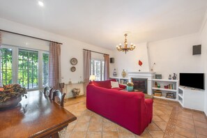 Un salon avec un canapé rouge, une cheminée, un téléviseur et un coin repas comprenant une table en bois.