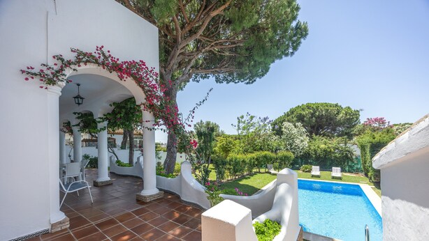 A poolside area with a clear view of the pool, white columns, and a covered patio with chairs. - Villa Jacaranda Chiclana, Private Pool and Barbecue (Chiclana de la Frontera)