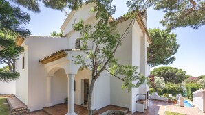 A white building with a tiled patio, a tree, and a pool. - Villa Jacaranda Chiclana, Private Pool and Barbecue (Chiclana de la Frontera)