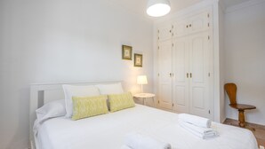 A neatly made bed with white linens, a bedside lamp, and a wooden chair. - Villa Jacaranda Chiclana, Private Pool and Barbecue (Chiclana de la Frontera)