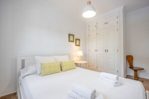 Ein ordentlich bezogenes Bett mit weißen Leinen, eine Nachttischlampe und ein Holzstuhl.