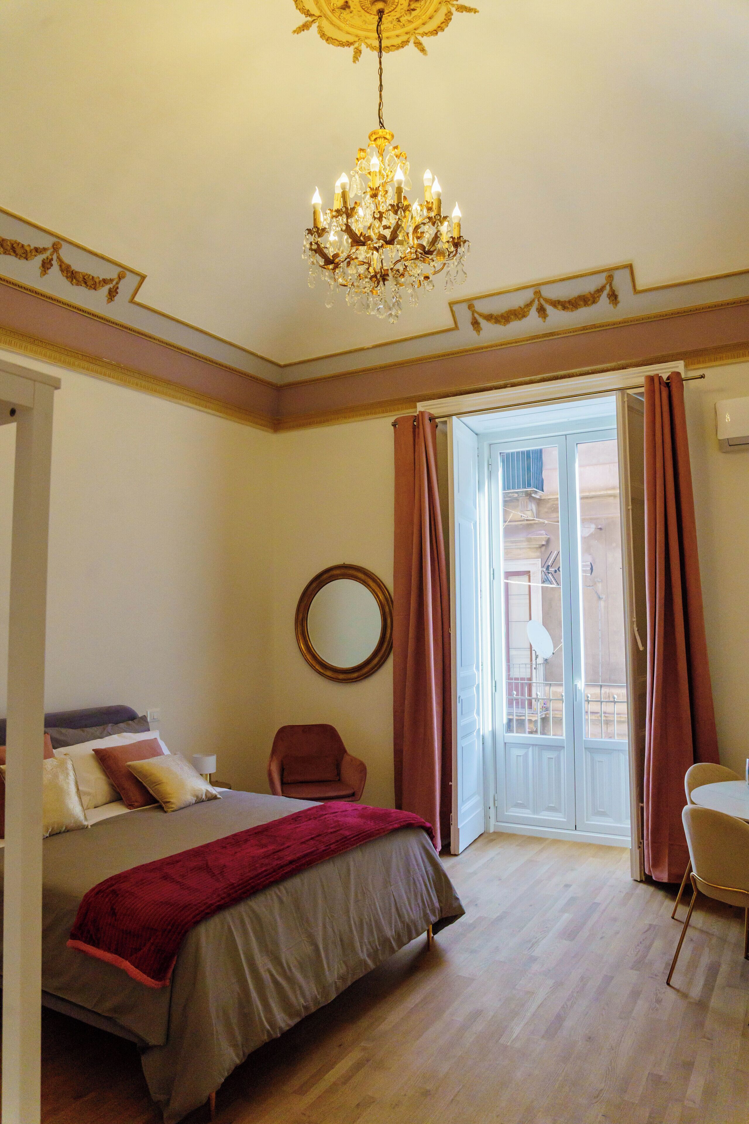 Ein Schlafzimmer mit einem Bett, einem Sessel, einer Chandelierleuchtre und einer Tür, die auf einen Balkon führt.