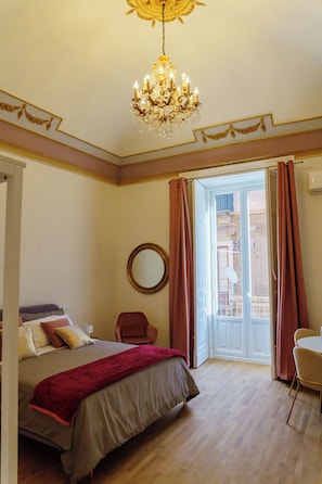 Ein Schlafzimmer mit einem Bett, einem Sessel, einer Chandelierleuchtre und einer Tür, die auf einen Balkon führt.