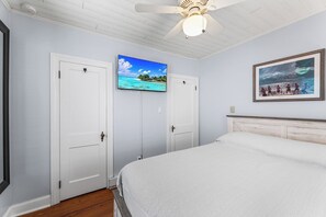 Ein Schlafzimmer mit Bett, Deckenventilator, Fernseher und zwei Türen.