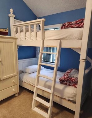 A bunk bed with a ladder, a white dresser, and a window.