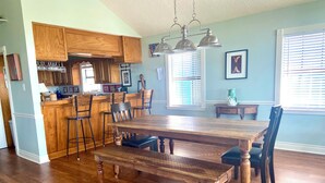 Uma sala de jantar com uma mesa e cadeiras de madeira, uma cozinha com armários de madeira e uma janela com persianas.