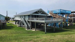 Um edifício à beira-mar com um alpendre coberto, escadas e uma estrutura azul nas proximidades.