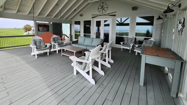 Um deck ao ar livre coberto com cadeiras Adirondack brancas, um sofá e uma mesa.