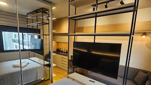 Quarto de hotel moderno com cama, televisão, sofá e espelho.