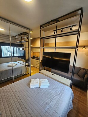Ein modernes Hotelzimmer mit Bett, Fernseher, Sofa und Spiegel.