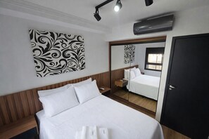 A hotel room with a bed, a bedside table, a mirror, and a wall-mounted air conditioning unit. - Studio Bem Localizado – Moema (São Paulo)