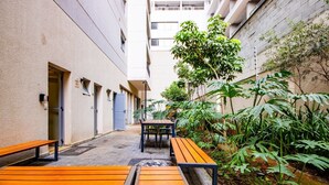 A courtyard with benches, a small table, and lush greenery. - Studio Bem Localizado – Moema (São Paulo)