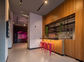 A modern kitchen with wooden cabinetry, a bar area with pink stools, and a visible counter. - Studio Aconchegante - Brooklin (São Paulo)