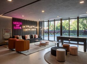 A modern lounge area with a neon sign, comfortable seating, and large windows offering a view of greenery. - Studio Aconchegante - Brooklin (São Paulo)