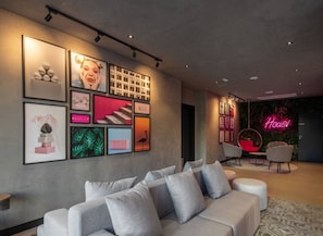 A modern hotel lobby with a grey sofa, framed artwork, and a neon sign. - Studio Aconchegante - Brooklin (São Paulo)