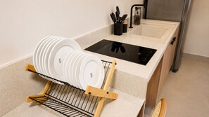 A kitchen with a dish rack, a black induction cooktop, and a stainless steel refrigerator. - BE CAJU FLATS  (Cajueiro da Praia)